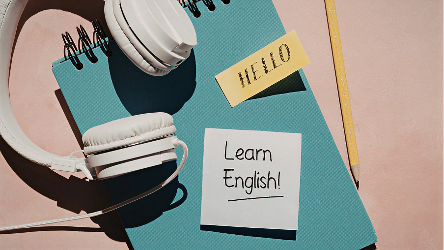 ヘッドフォンとノート。「Learn English!」という文字が書かれたポストイット。