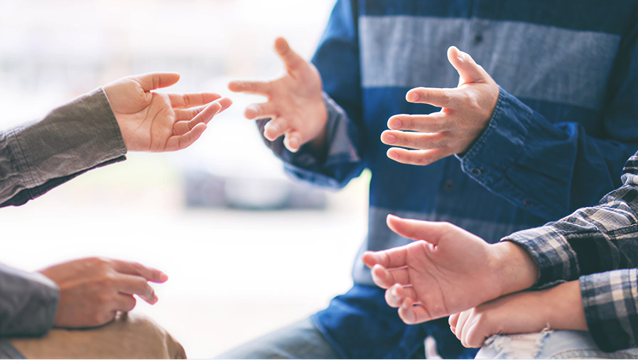 向かい合って座る3人の人物が英語で会話をしているイメージ。
